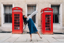 Woman With Arms Outstretched Balancing In Front Of Telephone Booth