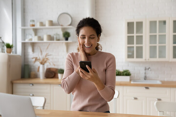 Wall Mural - Overjoyed millennial female look at cellphone screen triumph win online lottery on gadget. Smiling excited young Caucasian woman feel euphoric read good promotion or hiring news on smartphone.