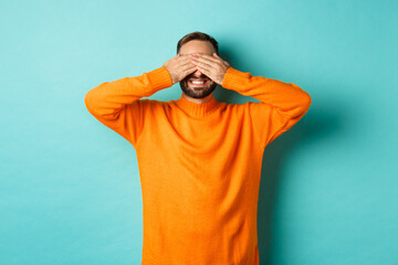 Happy bearded man waiting for surprise, shut ears and expeting gifts, standing over light blue background