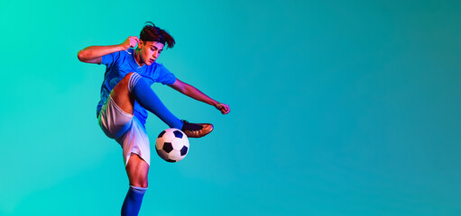 Wall Mural - Young man, male soccer football player training isolated on blue background. Flyer