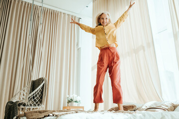 Stylish mature woman at her cozy home apartment. Energy jumping on the bed