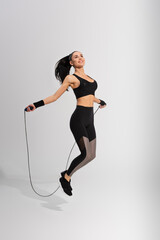 Wall Mural - full length of happy sportswoman exercising with skipping rope on grey