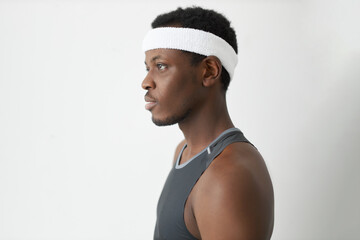 Wall Mural - Profile studio shot of young attractive Afro man wearing headband and tank top, posing with concentrated and focused face expression, trying to calm himself down and settle in for sports victory