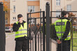 Two policemen stand in front of the entrance gate to the house