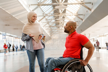 Muslim woman and disabled man talking to each other at train station