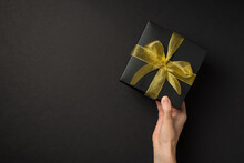 First Person Top View Photo Of Hand Holding Black Giftbox With Yellow Mesh Ribbon Bow On Isolated Black Background With Copyspace