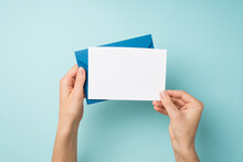 First Person Top View Photo Of Hands Holding Blue Envelope And White Card On Isolated Pastel Blue Background With Empty Space