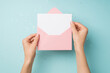 First person top view photo of hands holding open light pink envelope with white card over shiny sequins on isolated pastel blue background with blank space