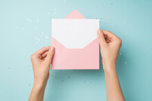First Person Top View Photo Of Hands Holding Open Light Pink Envelope With White Card Over Shiny Sequins On Isolated Pastel Blue Background With Blank Space