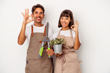 Young mixed race gardener couple isolated on white background cheerful and confident showing ok gesture.