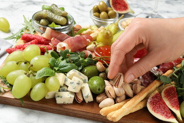 Wall Mural - Woman taking pistachio from board with different appetizers at white table, closeup