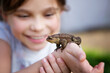 Cute girl looking at brown frog on hands. Childhood and researching concept.