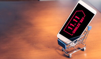 Smartphone with 11.11 message on screen inside a small shopping cart, singles day online shopping concept