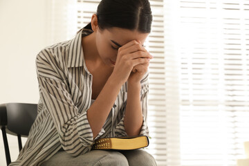 Beautiful young woman praying over Bible at home