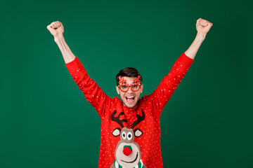 Poster - Portrait of attractive cheerful guy having fun rising hands up celebrating success winter eve isolated over green color background