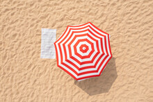 Striped Beach Umbrella Near Towel On Sand, Aerial View