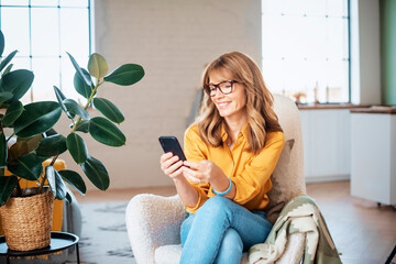 Smiling mature woman sitting in the armchair and text messaging