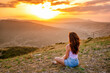 © KseniaJoyg - A young woman is sitting on the mountainside at sunset and enjoying the view of the mountains. The concept of an active lifestyle and peace.