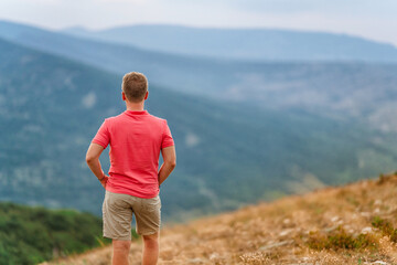 Wall Mural - A young blond man in a pink shirt conquered the top of the mountain at sunset. Beautiful mountain landscape with a gradient. The concept of enjoying nature.