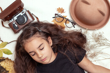 A beautiful little girl lies with closed eyes on a white blanket with autumn leaves