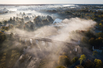 Poster - Venta Rapid waterfall, the widest waterfall in Europe and long red brick bridge in foggy, sunny autumn morning, Kuldiga, Latvia. Captured from above.