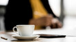 © Bangkok Click Studio - Close up shot of white hot coffee cup and small dish on meeting table near pencil while unidentified unrecognizable businessperson take short break after discussing and planning in blurred background