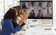 Close up shot of multicultural businessman businesswoman colleagues on teleconference on monitor screen greeting say hello to female officer staffs group in formal suit sitting waving hands together