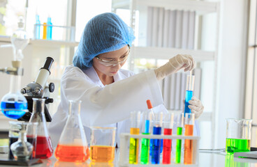 Sticker - Asian female professional scientist in white lab coat safety glasses hygiene cap and rubber gloves using glass stick stirring liquid sample in test tube on laboratory analysis research working desk