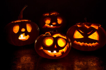 Halloween carved bright orange pumpkin jack lantern with different expressions of immotions on a dark textured background glow brightly in the dark