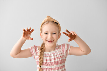 Sticker - Cute little girl with chocolate on hands and face against light background