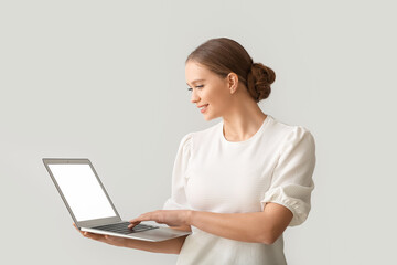Beautiful young woman holding laptop with blank screen on grey background