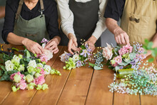 Close Up Of Three Florists Arraigning Flower Compositions On Wooden Table In Cozy Workshop, Copy Space