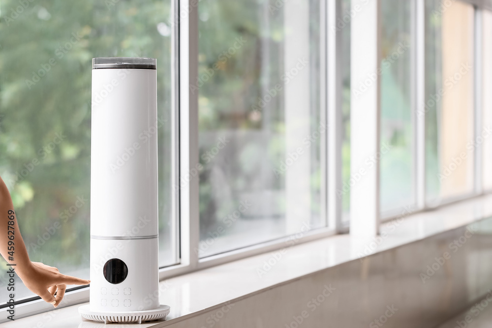 Woman switching on modern humidifier in room