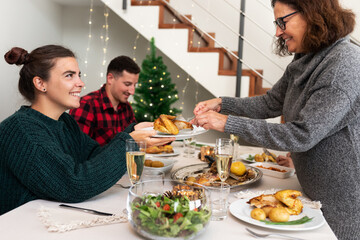 Wall Mural - Mother serves piece of roasted chicken to daughter. Happiness and togetherness. Christmas family dinner.