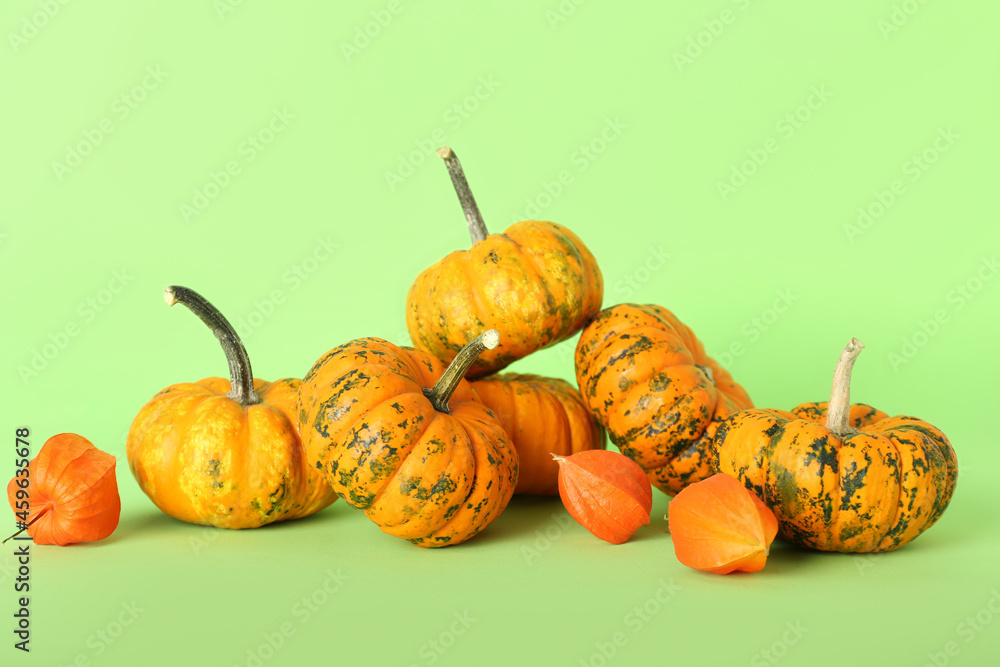 Many ripe pumpkins and physalis on color background