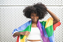 Afro Woman Wearing Pride Flag Standing In Front Of Metal Wall