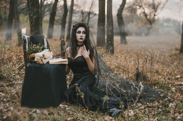 Brunette witch girl conjures in the forest conducts rituals with a fantasy skull nature magic in fire Halloween