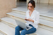 © Westend61 - Female freelancer using phone while sitting with laptop on staircase