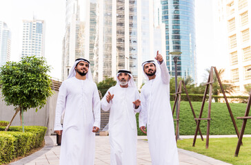 Wall Mural - Three business men walking in Dubai wearing traditional emirati clothes