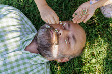 Girl Arranging Dandelion Flowers On Father's Face