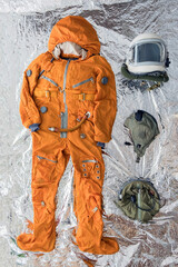 flat lay of astronaut orange space suit, space helmet and space suit accessories on silver backgroun