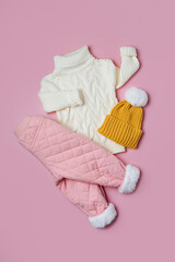 Wall Mural - White sweater and warm pants with hat on pink background. Stylish childrens outerwear. Winter fashion outfit