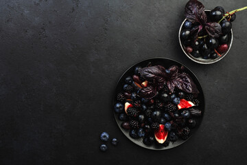 Wall Mural - Autumn blue and black berries fruit vegan salad: blueberries, blackberries, grapes, figs and purple basil with honey dressing on dark background, top view