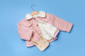 Wall Mural - Kids pink fur jacket hanging on a hanger with cute bag on blue background. Stylish childrens outerwear. Winter fashion outfit