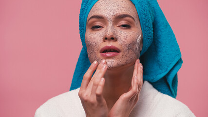 Wall Mural - woman with blue towel on head applying cosmetic scrub on face isolated on pink