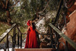 © Westend61 - Woman in little red riding hood costume looking up while standing in front of trees