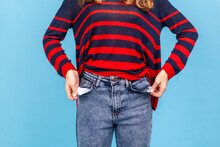 Portrait Of Unknown Faceless Anonymous Woman Turning Out Empty Pockets, Showing No Money Gesture, Wearing Striped Casual Style Sweater. Indoor Studio Shot Isolated On Blue Background.