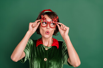 Wall Mural - Photo of pretty shocked young woman dressed elf costume deer glasses looking empty space isolated green color background