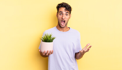 hispanic handsome man feeling extremely shocked and surprised. decorative plant concept