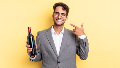 Wall Mural - hispanic handsome man smiling confidently pointing to own broad smile. wine bottle concept